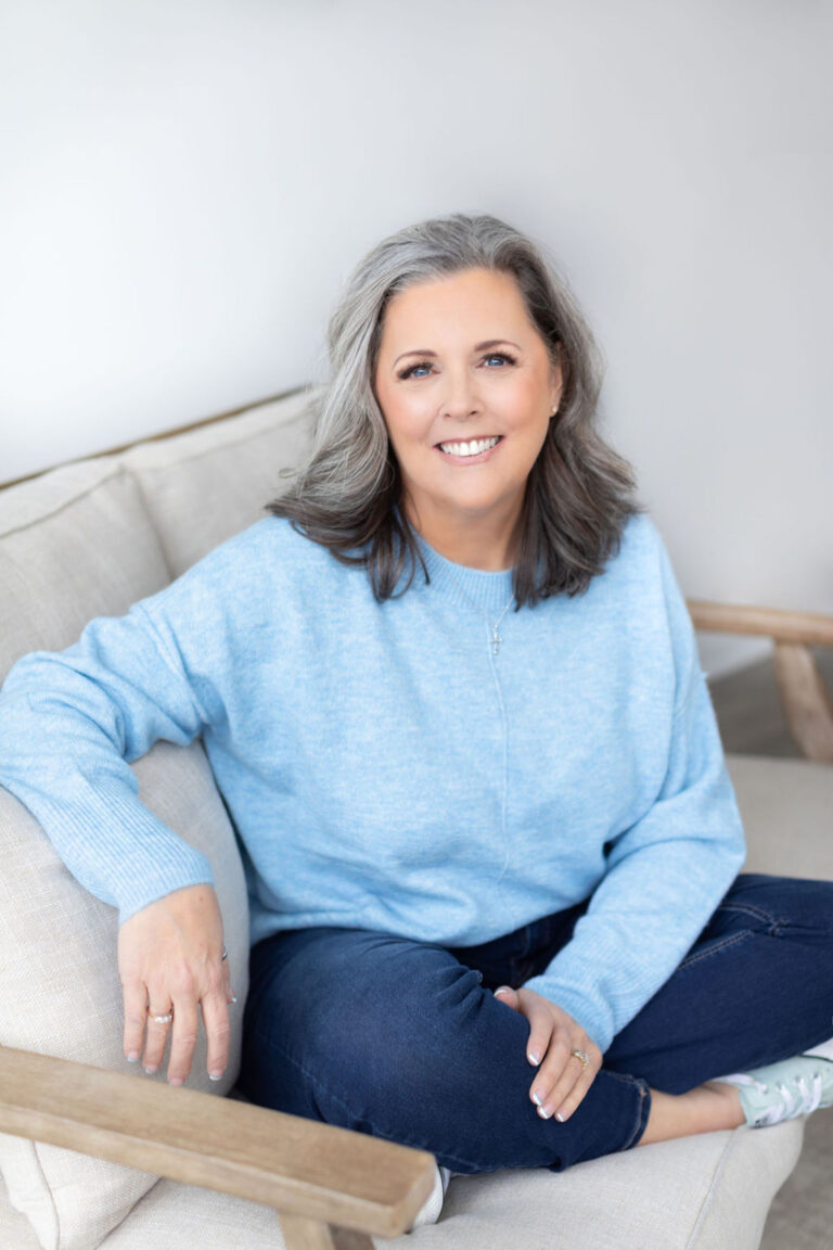 Smiling woman sitting on a couch in blue sweater.