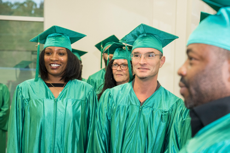 Graduates in green caps and gowns smiling